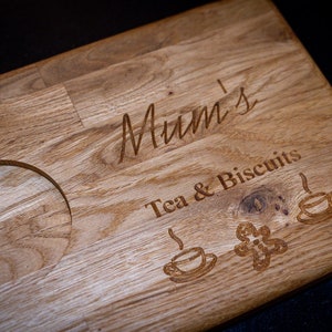 May include: A wooden serving tray with a cutout for a mug, engraved with the text "Mum's Tea & Biscuits" and three stylized images of teacups.