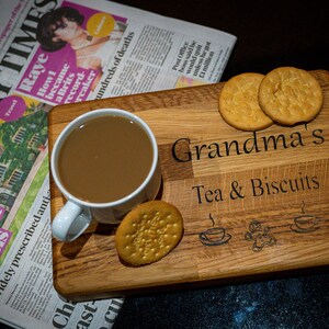 May include: A wooden serving tray with the text "Grandma's Tea & Biscuits" engraved on it. The tray has a cup of coffee and biscuits on it.