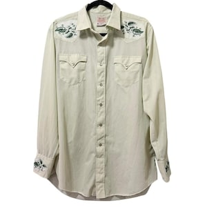 May include: A light green button-down shirt with long sleeves, two chest pockets, and a pointed collar. The shirt features embroidered green floral designs on the shoulders and cuffs. The shirt is hanging on a black hanger.
