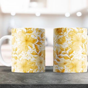May include: Two white ceramic mugs with a yellow floral pattern. The mugs have a white handle and are sitting on a gray countertop.