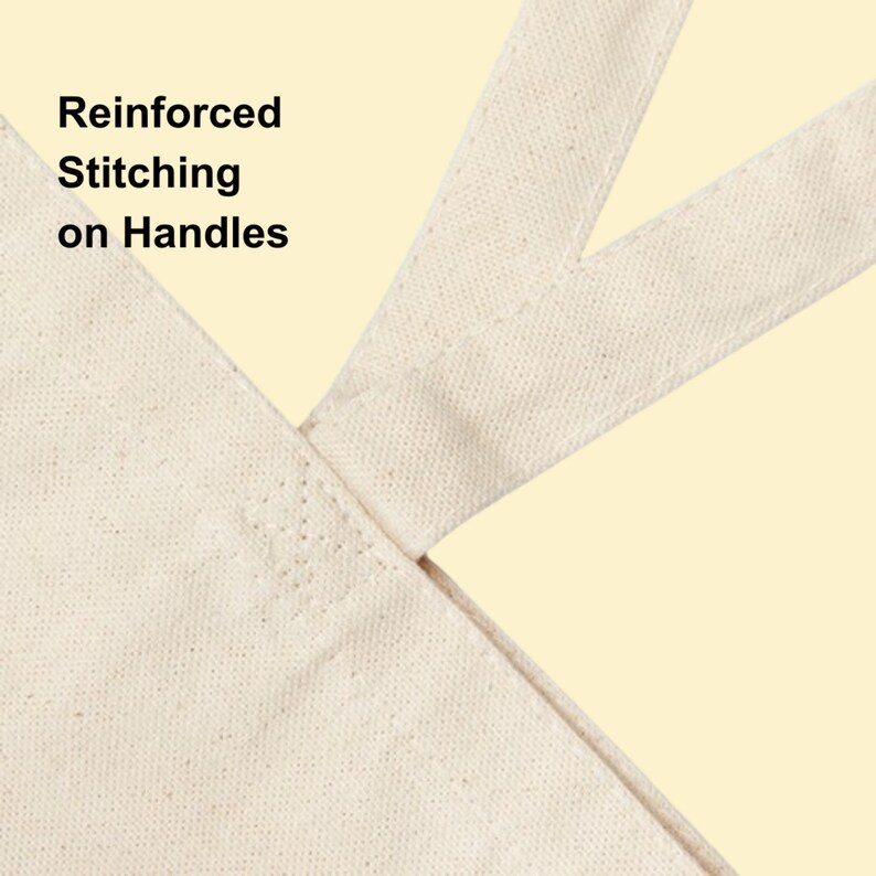 May include: A beige canvas tote bag featuring reinforced stitching on the handles. The fabric has a visible woven texture, and the handle attachment point displays a square pattern of heavy-duty thread reinforcement for added durability.