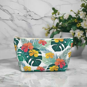 Tropical Floral Cosmetic Bag Front with Tropical pattern of hibiscus flowers and monstera palm leaves. T-bottom for more space. Durable zipper. Non-woven laminate interior for easy clean-up. Available in 2 sizes.

Bag on counter.