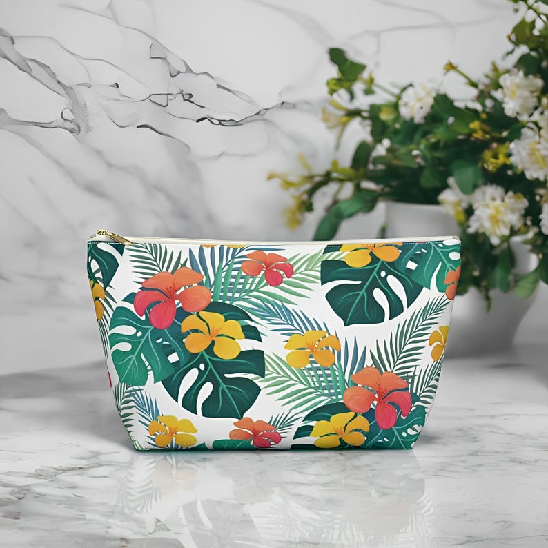 Tropical Floral Cosmetic Bag Front with Tropical pattern of hibiscus flowers and monstera palm leaves. T-bottom for more space. Durable zipper. Non-woven laminate interior for easy clean-up. Available in 2 sizes.

Bag on counter.