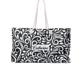 May include: A black and white tote bag featuring a repeating swirling leaf pattern and the name Catherine printed in a white rectangular box on the front. The bag has two thick white rope handles attached with knotted ends.