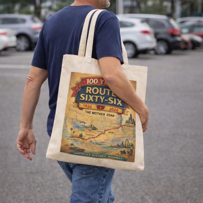 May include: A beige canvas tote bag featuring a graphic print of a Route 66 map. The design includes the text 100 YEARS ROUTE SIXTY-SIX 1926 2026 THE MOTHER ROAD AMERICA'S HISTORIC HIGHWAY, along with illustrations of a car, a city skyline, and a desert landscape.