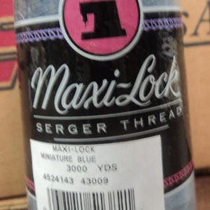 Peut inclure: Une bobine de fil à coudre sergé bleu Maxi-Lock. L'étiquette indique "Maxi-Lock Serger Thread", "Miniature Blue", "3000 YDS", "4524143 43009" et comporte un code-barres.