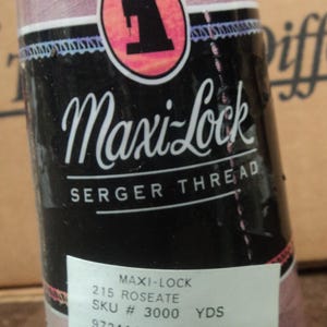 Peut inclure: Bobine de fil à surjeteuse Maxi-Lock de couleur rose tendre. L'étiquette présente le nom de la marque, les détails du produit et un code-barres. Le fil est enveloppé dans du plastique transparent.