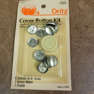 May include: A Dritz Cover Button Kit with six silver metal buttons, a white plastic button maker, and a silver metal pusher. The kit includes 6 buttons that are 5/8 inch (16 mm) in diameter. The packaging is beige with the Dritz logo and the words "Cover Button Kit" printed in black.