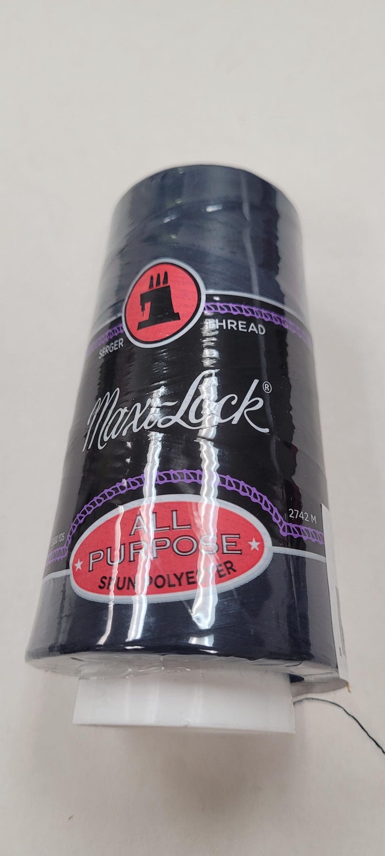 May include: A spool of Max Lock All Purpose Serger Thread in a dark blue color. The spool is labeled with the brand name, thread type, and length of 2742 meters.