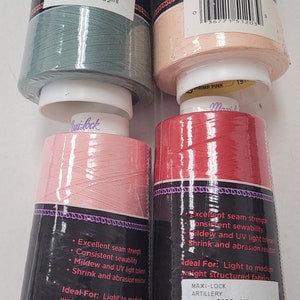 May include: Four spools of Maxi-Lock serger thread in different colors: seafoam green, shrimp pink, medium pink, and artillery red. Each spool has a label with the thread color, yardage, and barcode. The spools are stacked on top of each other.