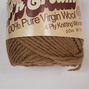 以下が含まれることがあります： 「'n Cream 100% Pure Virgin Wool 4 Ply Knitting Worsted 2 Ozs 56.7g」というラベルが付いた茶色の毛糸の玉
