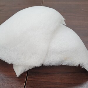 May include: Two white foam pads, likely for padding or cushioning, are stacked on top of each other on a wooden surface.