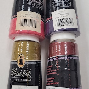 May include: Four spools of Maxi-Lock serger thread in various colors: dark pink, pansy, brass, and lauren. Each spool is labeled with the thread color, yardage, and a barcode. The spools are cylindrical with a black and red label.