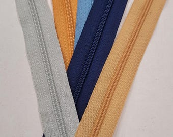 Könnte beinhalten: Eine Auswahl an offenen Reißverschlüssen in verschiedenen Farben: Grau, Orange, Hellblau, Marineblau und Beige. Die Metall-Reißverschlussschieber und Zähne sind auf jedem Reißverschluss sichtbar.