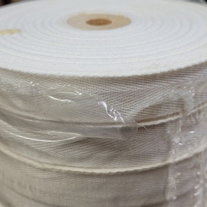 May include: A roll of white cotton twill tape, wrapped in clear plastic. The tape is woven with a herringbone pattern.