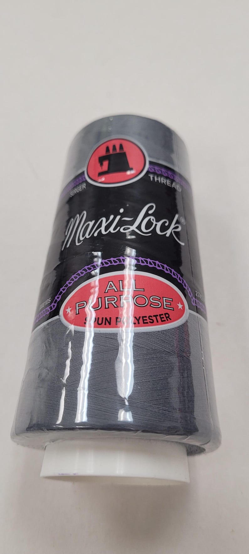 May include: A spool of Maxi-Lock All Purpose Spun Polyester thread in a dark gray color. The spool has a red and black label with the Maxi-Lock logo and the text "All Purpose Spun Polyester".