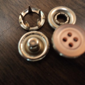 May include: A set of four gold-toned metal snap fasteners. The set includes two snap buttons, one snap socket, and one snap stud.