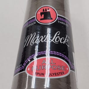 Peut inclure: Une bobine de fil Max Lock tout usage en polyester filé gris pour surjeteuse et machines à coudre. La bobine est étiquetée avec le nom de la marque et le type de fil.