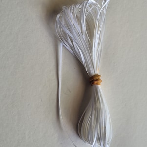 May include: A white satin ribbon, approximately 1/4 inch wide, is bundled together with a rubber band. The ribbon is white and has a slight sheen.