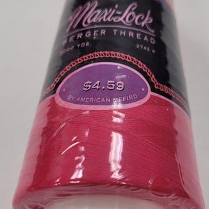 May include: A spool of pink Maxi-Lock serger thread by American & Efird. The spool is labeled with the text "Maxi-Lock Serger Thread", "3000 YDS", "2742 W", "$4.59", and "By American & Efird".