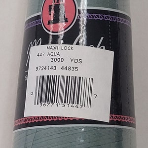 以下が含まれることがあります： 透明なプラスチックで包まれたアクア色のMaxi-Lockロックミシン糸のボビン。ラベルにはMAXI-LOCK、447 AQUA、3000 YDS、9724143 44835の文字とバーコードが記載されています。ボビンには白いプラスチック製のベースとピンクの縁取りがある黒いラベルが付いています。