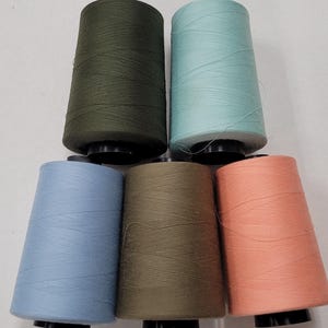May include: Six spools of thread in various colors, including green, blue, and orange. The spools are arranged in a pyramid shape.