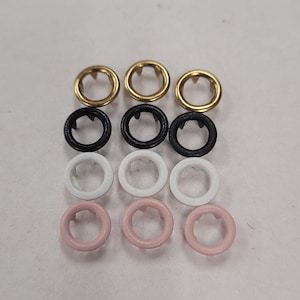 May include: Nine metal eyelets in three rows of three. The top row is gold, the middle row is black, and the bottom row is white and pink. The eyelets are circular with a small hole in the center.