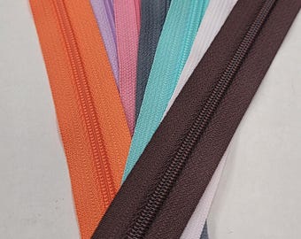 Könnte beinhalten: Sortiment an Reißverschlüssen in verschiedenen Farben, darunter Orange, Rosa, Lila, Türkis, Braun und Grau. Die Reißverschlüsse sind alle geschlossen und haben einen Metall-Schieber.