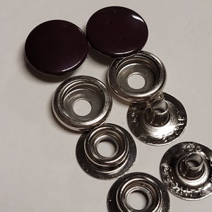 May include: A set of six snap fasteners, two dark brown plastic caps and four silver metal snaps. The snaps are designed for attaching fabric together.