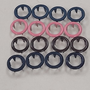 May include: Assortment of metal snap fasteners in three colors: dark blue, pink, and brown. The fasteners have a circular shape with a small hole in the center and three prongs on the underside.
