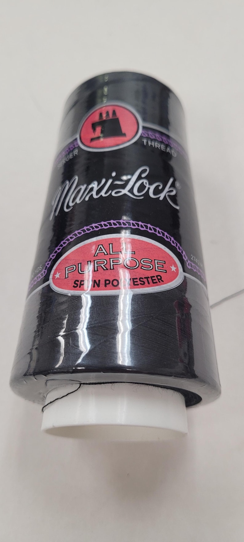 May include: A spool of black Maxi-Lock All Purpose spun polyester thread. The spool has a white label with the brand name and a red label that says "All Purpose Spun Polyester".