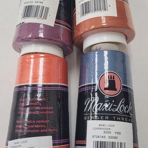 May include: Four spools of Maxi-Lock serger thread in various colors: Boysenberry, Hacienda, Toboggan, and Copenhagen. Each spool is labeled with the Maxi-Lock logo and product information. The thread is ideal for medium weight structured fabrics.