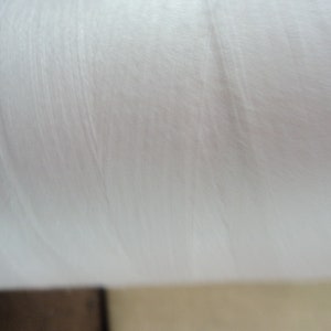 Peut inclure: Gros plan sur une bobine de fil blanc. Le fil est enroulé serré et a une texture lisse et soyeuse.