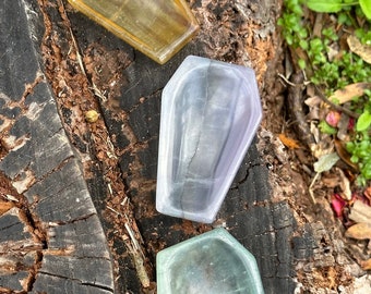 May include: Three coffin-shaped crystal dishes in different colors: yellow, purple, and green. The dishes are sitting on a tree stump.