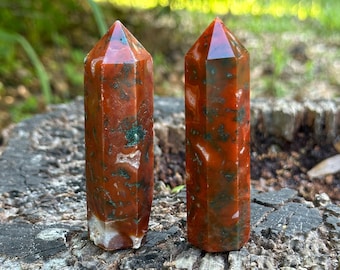 May include: Two red, green, and white carnelian crystal points on a tree stump. The points are about 2 inches long and have a natural, rough texture.