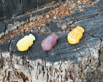May include: Three gummy candies shaped like bees, one yellow, one pink, and one orange, on a weathered tree stump.