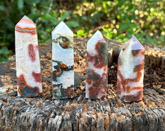 May include: Four white agate crystal points with red and green inclusions. The points are arranged in a row on a tree stump.
