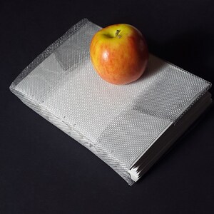 May include: A red and yellow apple rests on top of a stack of white paper, wrapped in a clear, textured plastic. The background is a dark, solid color. The apple is ripe and has a green stem.
