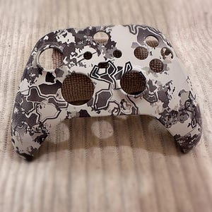 Op de afbeelding: Een witte en grijze camouflage-gepatenteerde videogamecontroller-behuizing. De behuizing heeft meerdere gaten voor knoppen en triggers.