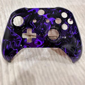 Puede incluir: Un mando de Xbox morado y negro con un diseño personalizado. El mando tiene un patrón de remolino con un fondo negro y detalles morados.