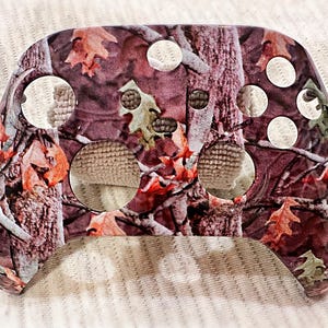 May include: A camouflage-patterned controller skin with a brown, green, and white design. The skin has multiple cutouts for buttons and other features.