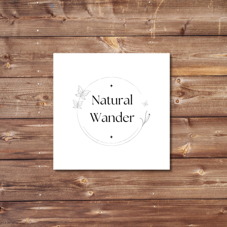 May include: A square white card with the words "Natural Wander" in a circular design, featuring delicate leaf and butterfly illustrations. The card is set against a rustic, brown wooden background.