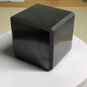 May include: A black, square-shaped, polished stone with a smooth surface.