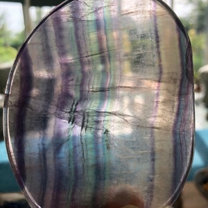 May include: A smooth, polished fluorite crystal with a translucent, iridescent appearance. The crystal has a rounded shape and displays a variety of colours, including purple, blue, and green.