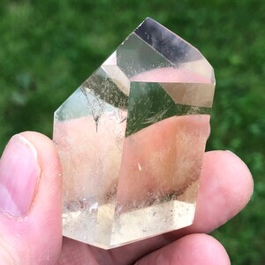 May include: A clear quartz crystal point with a light yellow hue. The crystal is faceted and has a natural, rough texture.