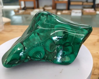 May include: A green malachite stone with a swirling pattern. The stone is polished and has a smooth surface.