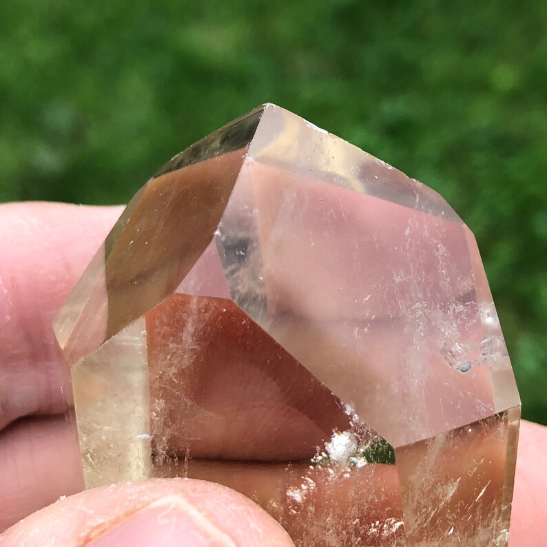 May include: A clear, faceted, quartz crystal with a light golden hue. The crystal is shaped like a pyramid with a flat base.