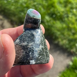 May include: A green, black, and pink carved stone with a triangular shape. The stone has a smooth, polished surface.