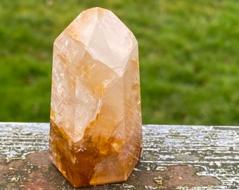 May include: A clear quartz crystal point with a golden brown inclusion. The crystal is polished and has a smooth, faceted surface.