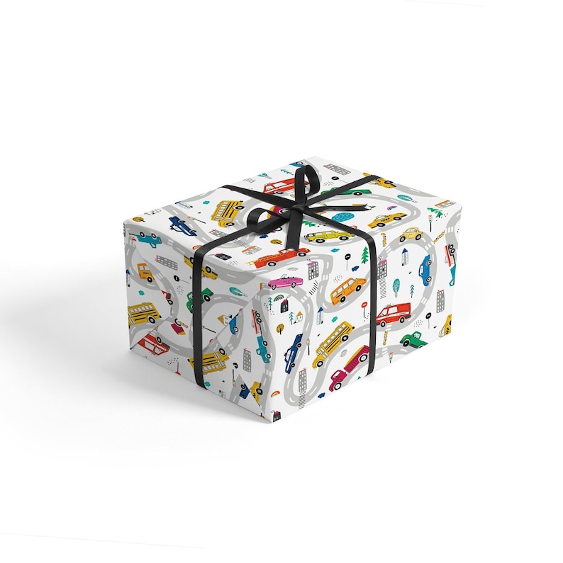 May include: A white gift box with a black ribbon. The box is wrapped in wrapping paper with a pattern of cars, trucks, and buses driving on a winding road. The pattern is in bright colors, including red, yellow, blue, green, and orange.